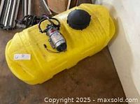 Yellow 25 gallon plastic spot sprayer tank with battery-powered pump and large black cap on top, wiring visible, placed on concrete floor.