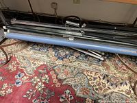 Two vintage roll-up movie projector screen cases and a black metal easel on a patterned carpet.