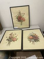 Three framed floral prints displayed on table and leaning against wall, light discoloration visible on prints.