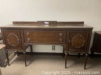 Full front view of antique wood buffet credenza showing carved wreath design on doors, two central drawers with round metal pulls, and tapered legs.