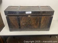 Front view of the antique wooden steamer trunk showing the domed lid, metal bands, worn wood surface, and keyhole lock.