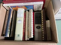 Photo of assorted hardcover books in a box showing various titles including cookbooks and literary works.