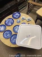 Top view of assorted blue and white porcelain plates and decorative items on a wooden table, including a white box labeled Lot 19
