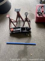 View showing the pair of red metal jack stands, black hydraulic floor jack, and blue handle lever laid on floor