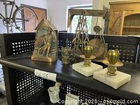 Photo showing oil derrick model, candlesticks on marble bases, brass coin bank, light fixture and face mug on black cart