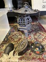 Cast iron lantern with a cage design, cast iron sad iron, and painted candlestick holder displayed on patterned rug.
