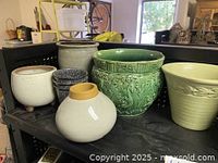 Overview of assorted ceramic flower pots on a black bench showing variety in size, color, and texture.