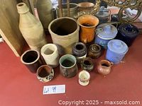 Photo showing a variety of ceramic stoneware items including crocks, a tall bottle, lidded jars, mugs, and decorative pottery on a table.