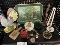Photo showing arranged small decor items on black surface including rooster figurine, decorative tray, boxes, candlesticks, spoons, and medallion.