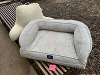 Overall view of the large rectangular dog bed in light gray fabric with quilting and raised bolsters positioned outdoors on a bench.