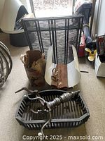 Cast iron firebox with hand crank in black metal fire grate holding embers or wood, along with fireplace screen and wood storage holder in background