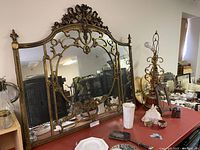 Full front view of ornate gilt wood mantel mirror on red table.