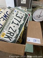 Box of old license plates showing a green and white Colorado plate with numbers and letters embossed, stacked with other plates.