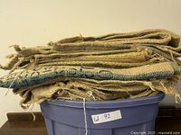 Stacked burlap coffee bags folded and placed on top of a large purple plastic tub labeled 'Lot 92'.