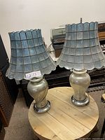 Pair of vintage lamps on round wooden table showing pearlescent bases and blue capiz lampshades