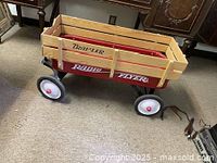 Red Radio Flyer wagon shown with removable Trav-Ler wood guard rails attached. Wagon has a red body, white wheels with black tires, and wood side rails.