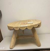 Front angle view of the small round cedar table showing the scalloped edge of the table top and three stout legs.