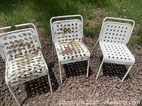 Three white metal mid-century modern outdoor chairs placed on a gravel surface showing significant rust and paint stripping mainly on seats and backs.
