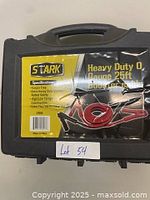 Closed black plastic carrying case with Stark brand label and product info, held closed with tabs. Label mentions heavy duty 0 gauge 25ft booster cable, specifications, and shows cable image.