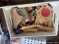 Wooden train track pieces and several Thomas the Tank Engine trains of various sizes inside a white tray.