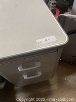 Close-up of the desk corner showing metal drawers with silver handles and gray laminated top surface.