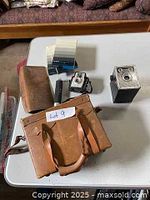 Lot overview showing cameras, film, and leather bag from above on a white tabletop.