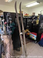 Full view of two wooden cross country skis standing upright next to golf clubs showing size and shape.