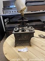 Vintage Crescent cast iron stove salesman sample table lamp with askew lamp fitting on wooden table.