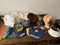 All hats displayed together on wooden surface including visors, baseball caps, crochet hats, and newsboy caps