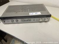 Front and top view of vintage Hitachi HTA-2 AM/FM stereo amplifier receiver on a table, showing control knobs and ventilation grills on top.