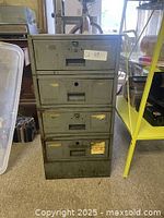 Front view of the stacked metal storage boxes showing four drawers with label slots and keyholes. Visible wear and rust present.
