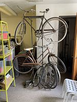 Overall view of two vintage bicycles (Raleigh Sports and Rudge Sports) on a metal rack with assorted wheels on the floor beside them