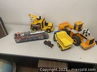 Full lot photo showing all five toys: the Piston Silver Mountain tin train, Fisher Price tow truck, Epic Trucking dump truck, Bright Industries Caterpillar front end loader, and a small cast iron pickup truck