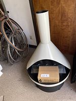 Front view of white metal freestanding TerraFlame gel fireplace with conical chimney, circular base and TerraFlame gel fuel box in bowl.