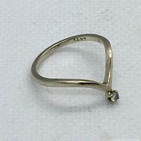 Side angle of 14k gold ring with open V-shape and small clear stone.