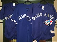 Three blue Blue Jays jerseys hanging side by side showing fronts