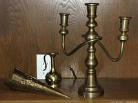 Brass three-arm candelabra, small brass pitcher, and decorative brass horn on wood background