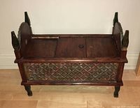 Front view of the carved wooden bench showing the hinged top and carved painted front panel.