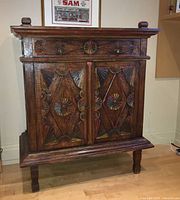 Front view of the carved and painted small armoire showing symmetrical geometric carvings and painted accents in red, green, and yellow.