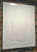 Front view of white marble relief panel mounted on a brick wall, featuring two figures embracing wearing fur-trimmed winter clothing.