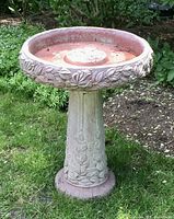Full outdoor view of the Henri Studio cast stone bird bath with decorative leaf patterns on bowl rim and pedestal base, showing overall condition and scale.