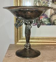 Side view of the wide shallow bowl and ornate pedestal stem with grapevine details and hanging grape clusters