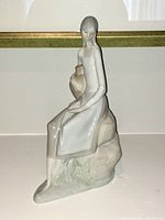 Front view of Lladró porcelain figurine of a woman seated on rock holding vase.
