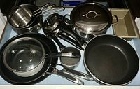 Overview of cookware items including frying pans, saucepans, steamer, lids, and bowls arranged in a drawer