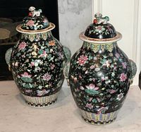 Pair of large black pottery ginger jars with floral designs and turquoise handles, gold rings and lids topped with foo dog figurines.
