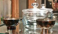 Photo showing pair of silver Sabattini bowls with polished reflective finish and glass lidded dish in the background on glass shelf