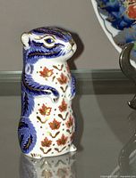 Front side view of the Royal Crown Derby squirrel figurine showing blue feather detailing and red/gold leaf accents on white porcelain.
