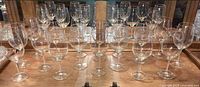 Set of 17 clear wine glasses arranged on a wooden surface in front of a mirrored cabinet.