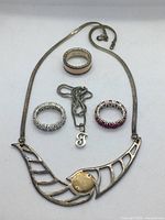 Full view of necklace, pendant chain with letter 'J', and three rings.