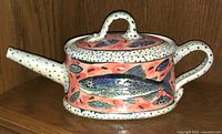 Front side view of the vintage Kuzyk Mackie Newfoundland art pottery teapot showing fish design, cylindrical shape, and speckled white background.